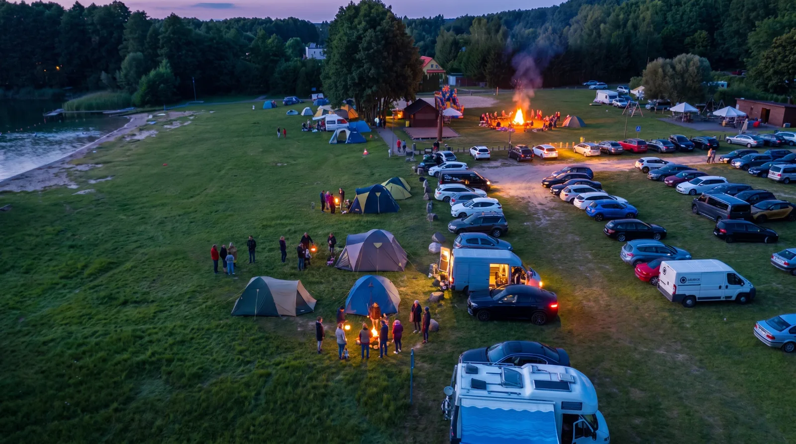 Wieczorne ognisko na polu biwakowym nad jeziorem, namioty i kampery
